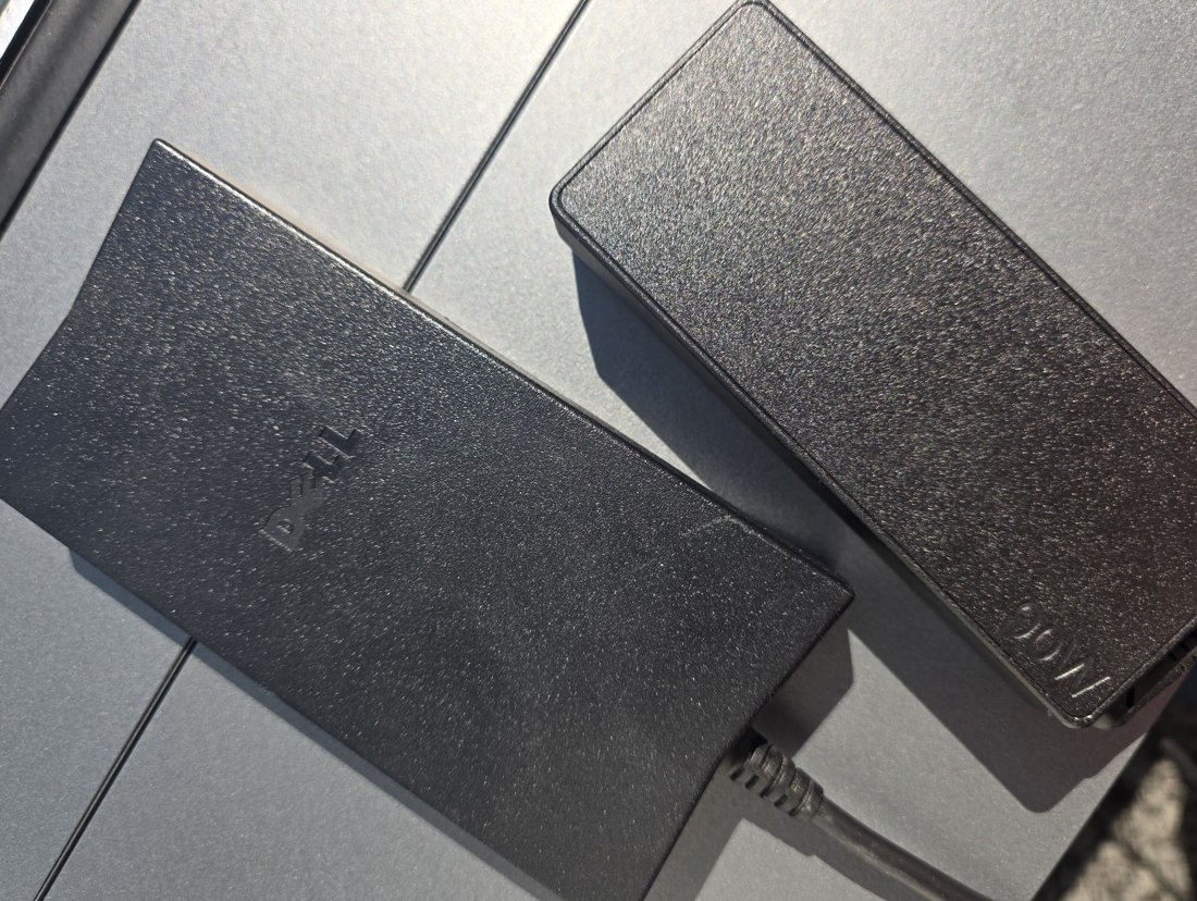 Dell laptop power brick beside a 90 W adapter on a grey desk