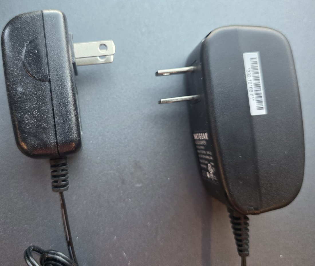 Two plug-in wall wart power adapters, one generic and one Netgear